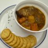 Crackers on a white plate alongside a white bowl of beef pot roast with potatoes and carrots