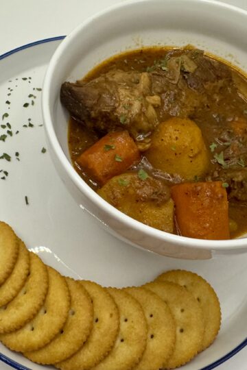 Crackers on a white plate alongside a white bowl of beef pot roast with potatoes and carrots