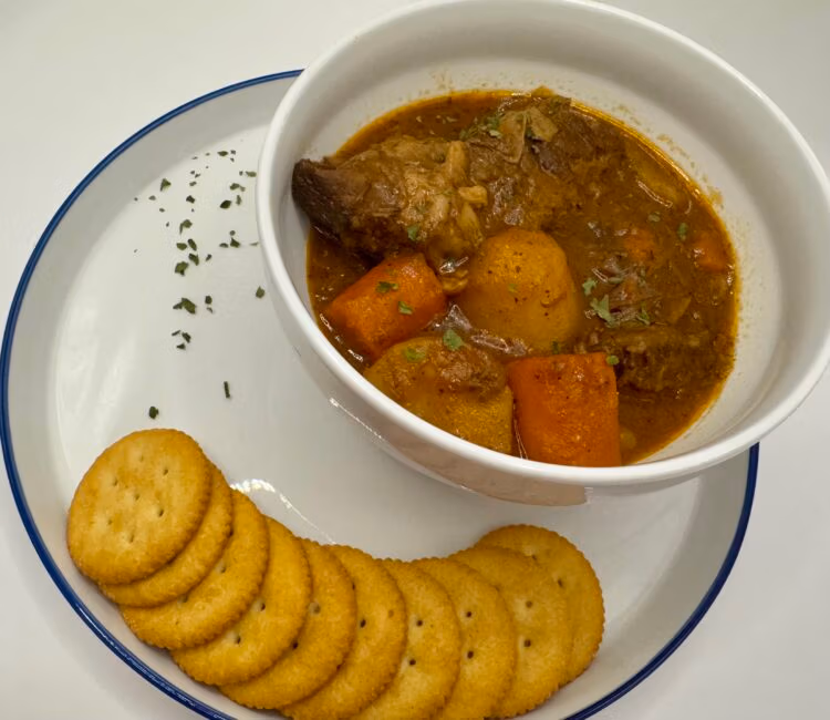 Crackers on a white plate alongside a white bowl of beef pot roast with potatoes and carrots