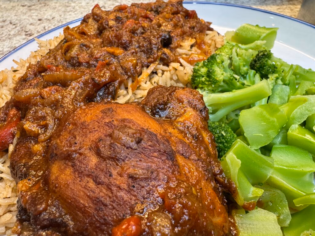 Jamaican brown stew chicken served with Jamaican rice and peas and steamed broccoli on a white plate