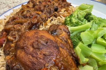 Jamaican brown stew chicken served with Jamaican rice and peas and steamed broccoli on a white plate