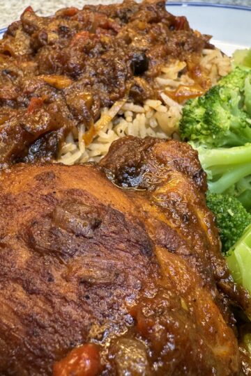 Jamaican brown stew chicken served with Jamaican rice and peas and steamed broccoli on a white plate