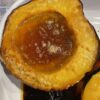 Two halves of golden roasted acorn squash with bubbling maple syrup and butter, caramelized edges, and a fork resting beside them.