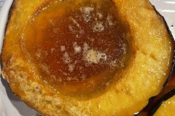 Two halves of golden roasted acorn squash with bubbling maple syrup and butter, caramelized edges, and a fork resting beside them.