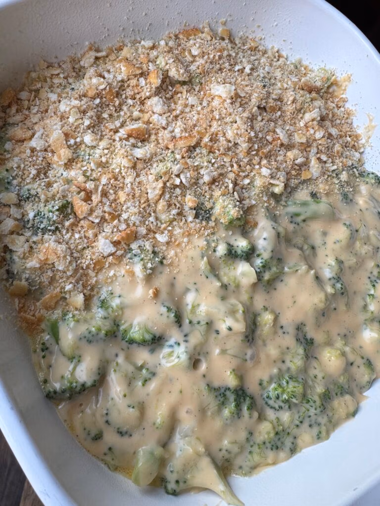 A white Casserole dish with creamy cheesy broccoli and cheddar with half topping of Ritz Crackers