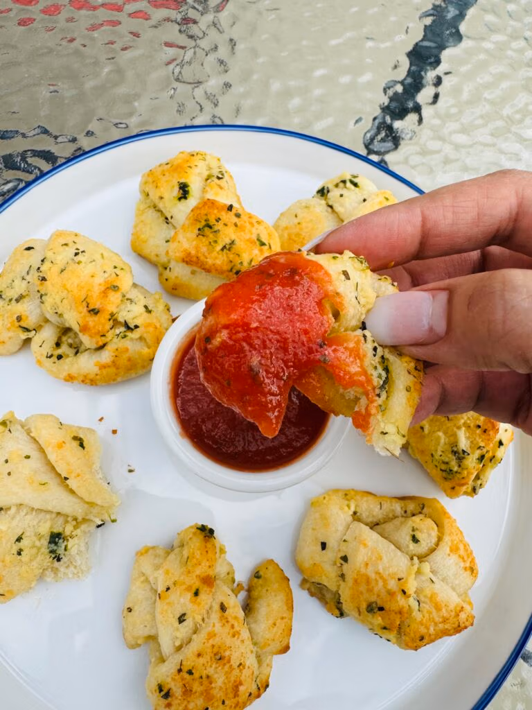 A crispy golden garlic knot dipped in marinara sauce