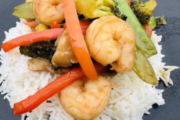 Shrimp Broccoli and Snow Peas Stir Fry on to of a bed white rice on a black plate
