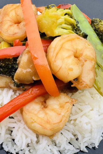 Shrimp Broccoli and Snow Peas Stir Fry on to of a bed white rice on a black plate