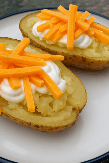 Baked Potatoes on a White plate topped with sour cream and cheese