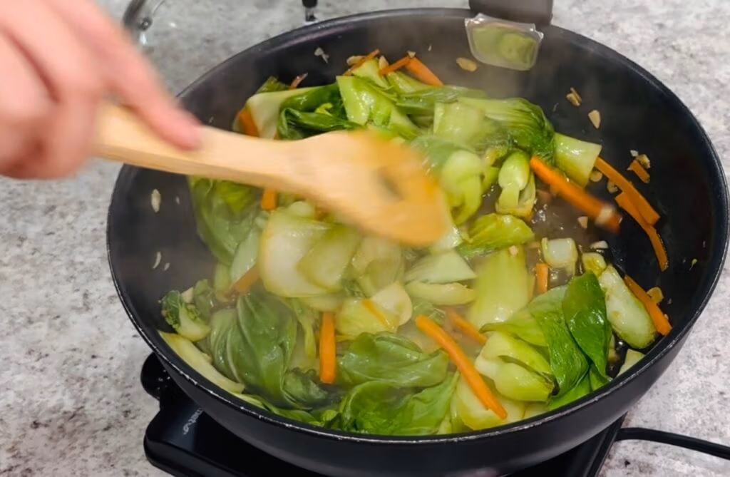 fresh chopped bo choy and julienned carrots sauteeing in a pan