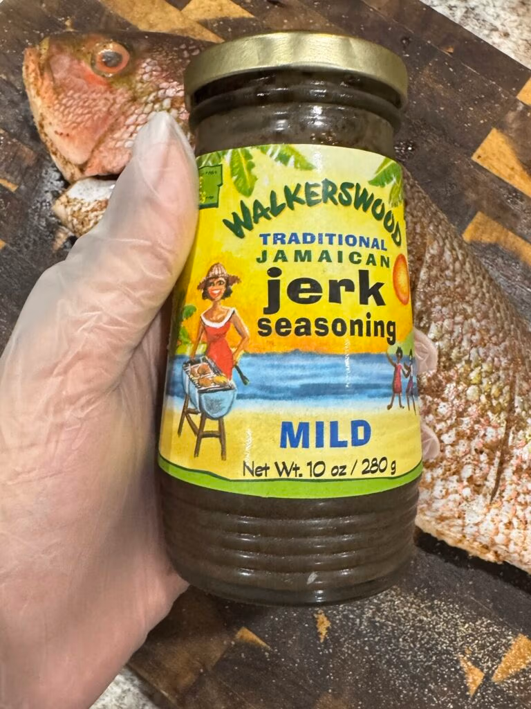 Gloved Hand holding a bottle of Walkerswood Jamaican Jerk Seasoning Mild