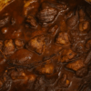 a closeup of greek lamb stifado, a stew of lamb chunks in a deep rich sauce