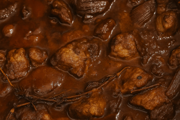 a closeup of greek lamb stifado, a stew of lamb chunks in a deep rich sauce