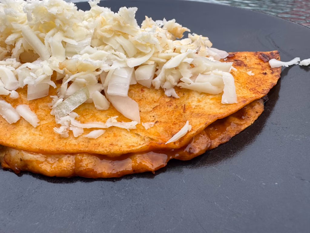 Slow cooker beef birria on a black plate with a heap of oaxaca cheese on top.