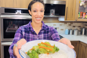 Camille of Camilles Comforting Cuisine holding a plate sauteed bok choy with white rice.